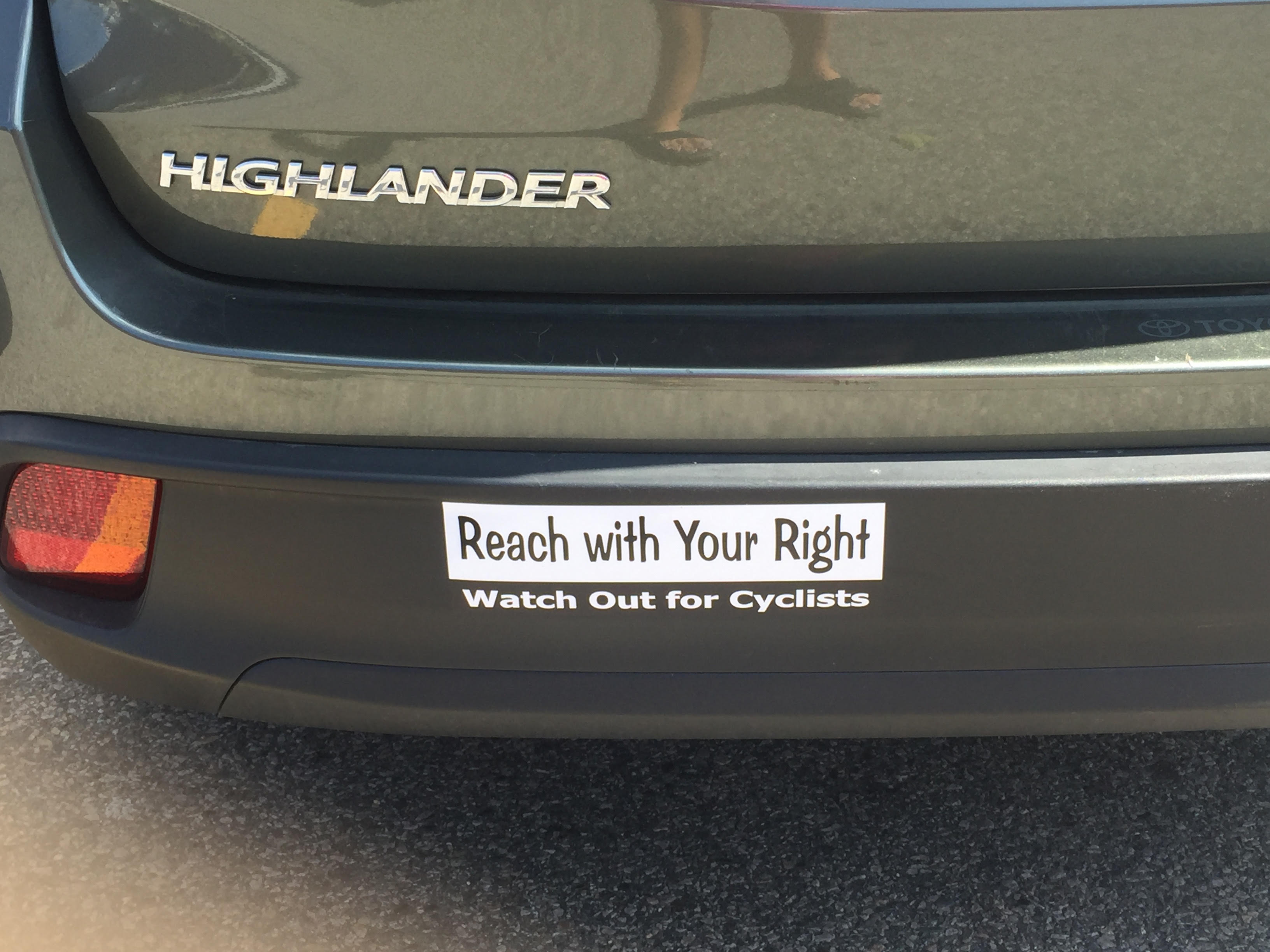 Image of car bumper with sticker reading "Reach with Your Right, Look Out for Cyclists". A school teacher in Oregon starts her own campaign backed on the far hand anti dooring method, August 2017.