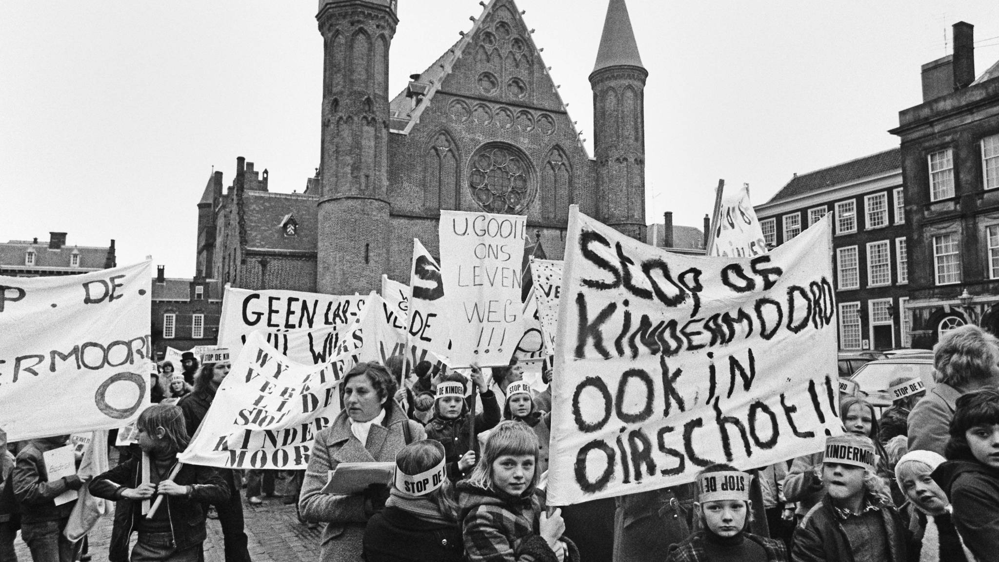 Stop de Kindermoord protest in Netherlands with children, parent in town square.